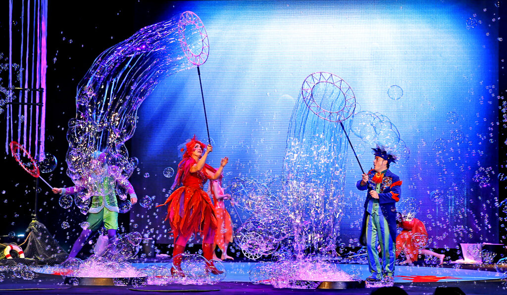 Group of performers on a stage surrounded by bubbles.